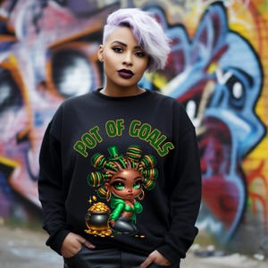 May include: Black sweatshirt with a green, gold, and brown cartoon illustration of a woman with a pot of gold. The text "POT OF GOALS" is printed on the sweatshirt.
