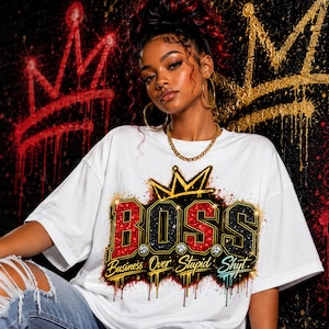 May include: A white short-sleeved t-shirt featuring a graphic print of a gold crown above the word BOSS in red and black glittery letters. Below the text, the phrase Business Over Stupid Shyt is written in a stylized font with paint drips.