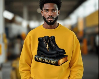 May include: Mustard yellow sweatshirt featuring a graphic of black boots, a gold cross necklace, and a book with the text "PRAYER WARRIOR". The boots are placed on top of the book. The sweatshirt has a crew neck and long sleeves.