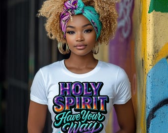 May include: A white t-shirt with the text "HOLY SPIRIT Have Your Way" in a colorful, stylized font. The person in the image is wearing a patterned head wrap and large gold hoop earrings. The background is a colorful wall with graffiti.
