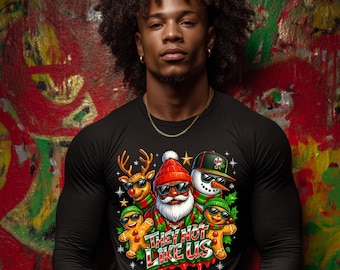 May include: Black long-sleeve shirt with a Christmas graphic featuring Santa, a reindeer, a snowman, and gingerbread men wearing sunglasses. The text "THEY NOT LIKE US" is displayed below the characters. The background is a colorful graffiti wall.