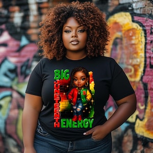 May include: Black t-shirt with a graphic of a cartoon Black girl with braids, wearing a red and green jacket, standing in front of a brick wall with the words "BIG JUNETEENTH ENERGY".