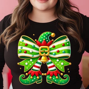 Puede incluir: Una camiseta negra de manga larga con un lazo verde y blanco con un diseño de pierna de elfo a rayas rojas y blancas. El lazo tiene una hebilla dorada y una campana.