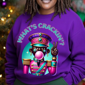May include: Purple sweatshirt with a graphic of a cartoon nutcracker with a pink bubble and the text "What's Crackin'?"