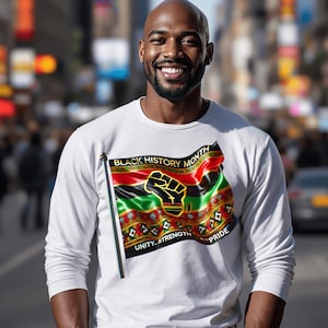 May include: White long-sleeve shirt featuring a flag design with the text "BLACK HISTORY MONTH", a raised fist, and the words "UNITY, STRENGTH, PRIDE". The flag design incorporates red, green, black, and gold colors.