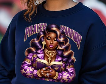 Peut inclure: Sweat-shirt bleu marine avec un motif représentant une femme aux cheveux violets et blonds tenant un livre avec les mots "PAYKE" sur la couverture. Le texte "PRAYER WARRIOR" est écrit en lettres dorées autour de la femme.