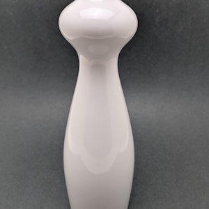 Puede incluir: Un jarrón alto de cerámica blanca con una sección media bulbosa y un cuello delgado. El jarrón tiene un acabado brillante y una silueta suave y curvada. Un artículo decorativo.