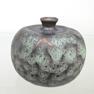 Op de afbeelding: Een ronde keramische vaas met een smalle hals en een getextureerd oppervlak. De afwerking heeft een gevlekt patroon van donker antracietgrijs en gedempt mintgroen, met subtiele metallic bronzen accenten op de verhoogde delen van het glazuur.