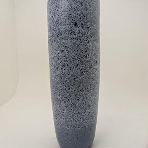 Op de afbeelding: Een hoge, cilindervormige vaas met een gespikkelde, getextureerde oppervlakte. De vaas heeft een kleurenschema met een verloop, van donkerder blauw aan de basis naar lichter blauw aan de bovenkant. De vaas is ongeveer 30 cm hoog.