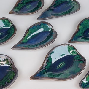 May include: Set of eight small ceramic leaf-shaped dishes with a blue and green glaze. The dishes have a metallic sheen and are perfect for serving small snacks or condiments.