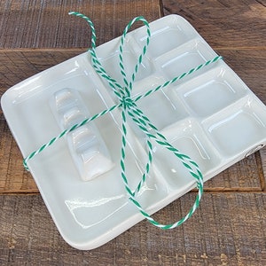 May include: A white ceramic paint palette with nine separate wells, including a long, rectangular well. The palette is tied with green and white twine.