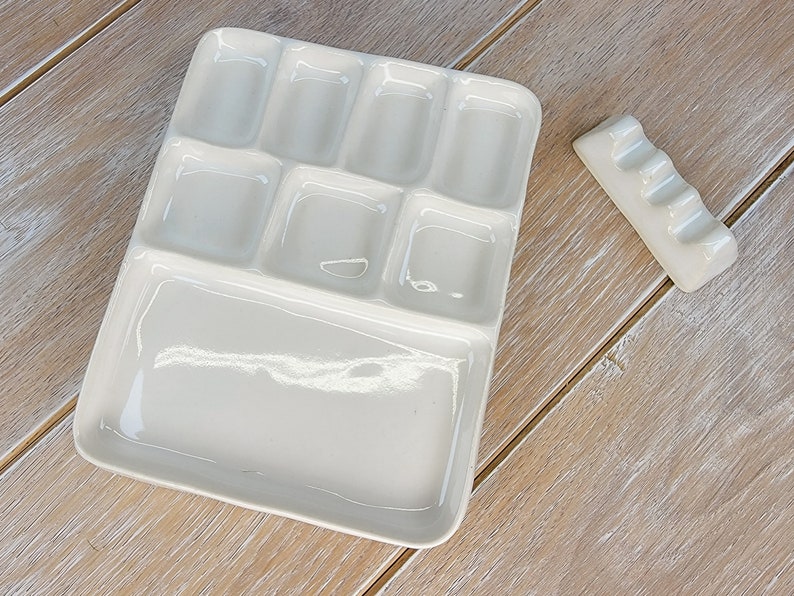 May include: A white ceramic paint palette with nine wells, including a large well for mixing. A small white ceramic brush holder with four slots is also included.