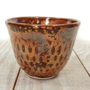 May include: A small, brown ceramic bowl with a speckled glaze. The bowl has a rounded shape and a slightly flared rim.