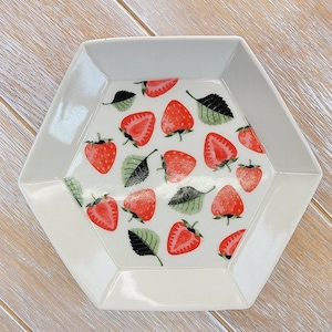 May include: A white hexagonal ceramic dish with a glossy finish features a pattern of red strawberries and green leaves.