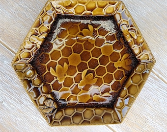 Puede incluir: Plato de cerámica hexagonal con diseño de panal y abeja. El plato está esmaltado en tonos marrones y dorados, con detalles de panal y abeja en relieve. El plato mide aproximadamente 20 cm de ancho.