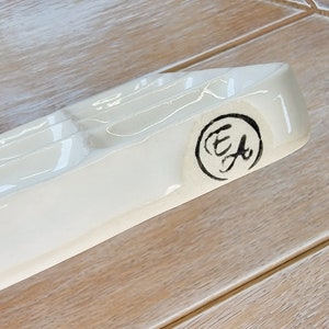 May include: White ceramic paint palette with six wells and a black circular stamp with the letters "E.F." inside.