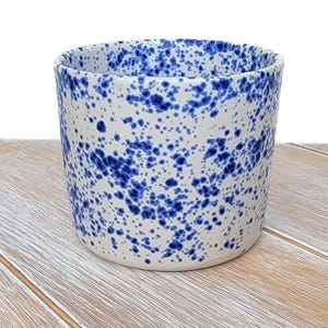 May include: A white ceramic planter with a blue speckled glaze. The planter is cylindrical in shape and has a smooth, rounded rim.