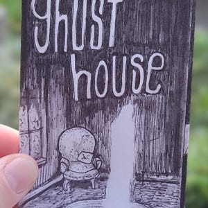 May include: A black and white illustration of a room with the words "ghost house" in white lettering. The room features an armchair, a fountain, and a window. The artist's signature is in the bottom left corner.
