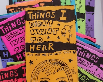 May include: A stack of small, brightly colored books with the title "Things I Didn't Want To Hear But Did Me The Most Good" in black lettering. The books have a cartoon illustration of a person with yellow hair and large eyes.