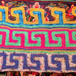 May include: A colorful crocheted blanket with a geometric pattern. The blanket is made with different shades of blue, green, pink, yellow, and orange yarn.