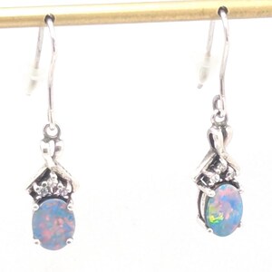 May include: A pair of silver-toned dangle earrings. Each earring features an oval, iridescent opal gemstone. The gemstones are set in a decorative silver setting with small, clear accent stones. The earrings hang from a simple hook.