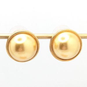 以下が含まれることがあります： 丸い真珠のようなデザインのゴールドスタッドピアス。ピアスは白い背景に金色のスタンドに展示されています。ピアスはシンプルでエレガントなデザインです。