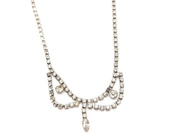 May include: A silver necklace with a teardrop pendant and a delicate, curved design. The necklace is made of small, clear rhinestones.