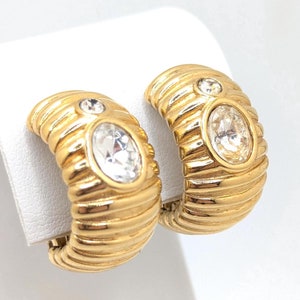 Puede incluir: Un par de pendientes de aro de oro con detalles de cristal transparente. Los pendientes tienen un diseño texturizado y acanalado.