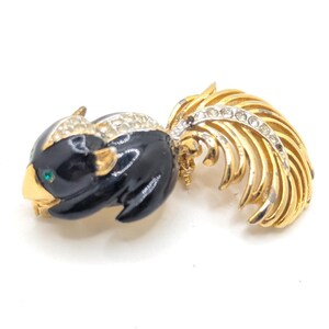 Könnte beinhalten: Eine goldfarbene Brosche mit einem schwarzen Emaille-Eichhörnchen-Design. Das Eichhörnchen hat grüne Augen und einen langen, gefiederten Schwanz mit klaren Strasssteinen.