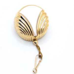 May include: A gold-coloured, shell-shaped pendant with a white interior. The pendant is attached to a gold-coloured chain with a clasp.