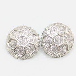 May include: A pair of silver tone earrings with a geometric honeycomb design. The earrings are round and have a textured surface.