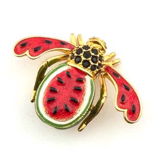 以下が含まれることがあります： 金色の金属製ブローチ。蜂の形をしており、蜂の体は赤、黒、緑のエナメルで描かれたスイカのスライスです。羽は黒い斑点のある赤色で、頭には黒いラインストーンが飾られています。