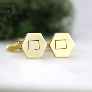 May include: A pair of gold cufflinks with a square design. Each cufflink is a hexagon shape with a square in the centre.