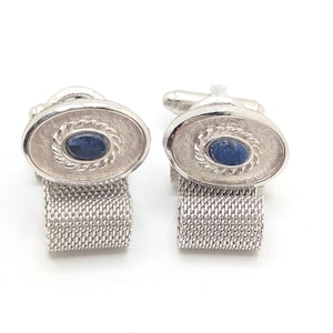 May include: A pair of silver cufflinks with a blue oval stone set in a silver frame. The cufflinks have a mesh design on the back.