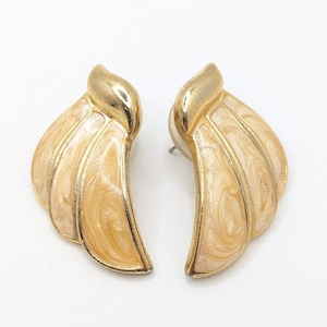 May include: A pair of gold tone earrings with a cream swirl design. The earrings are shaped like a fan or a wing.