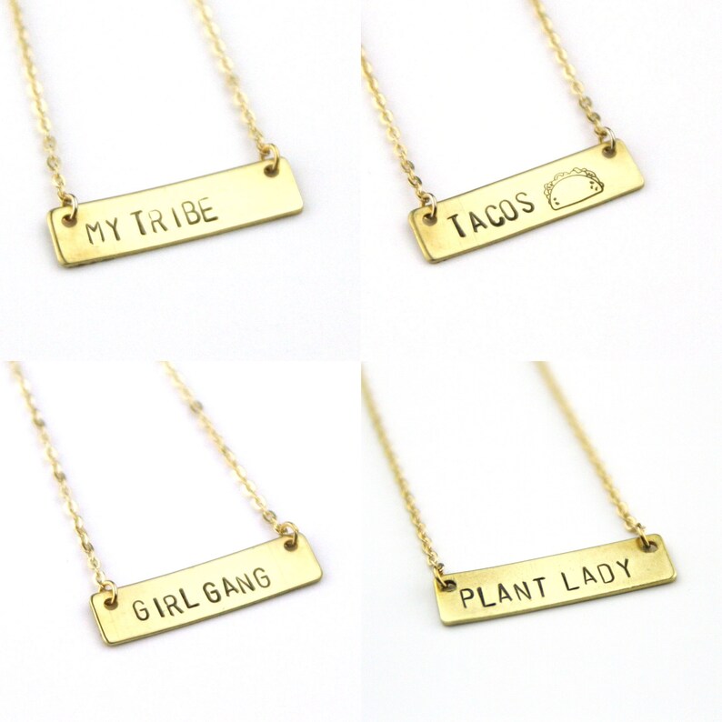 K&ouml;nnte beinhalten: Vier goldene Halsketten mit verschiedenen Inschriften auf rechteckigen Anh&auml;ngern. Die Anh&auml;nger tragen die Inschriften "My Tribe", "Tacos", "Girl Gang" und "Plant Lady".