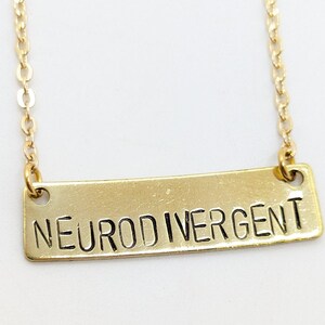 K&ouml;nnte beinhalten: Eine goldene Kettenkette mit einem rechteckigen Anh&auml;nger, auf dem in schwarzen Buchstaben "Neurodivergent" steht.