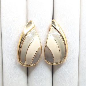 May include: A pair of gold tone earrings with a white and grey enamel design. The earrings are shaped like teardrops.