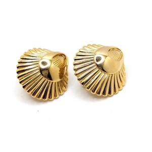 May include: A pair of gold-coloured stud earrings. Each earring has a rounded top and a ridged, radiating design. The earrings are set against a white background, highlighting their metallic sheen and intricate details.