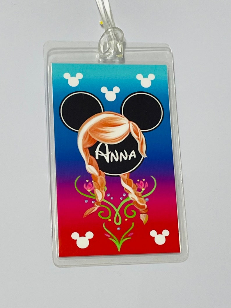 May include: A clear plastic luggage tag with a colourful design featuring a Mickey Mouse head with Anna from Frozen's hair and the name "Anna" written in white. The background is a gradient of blue, purple, and red with white Mickey Mouse ears at the top and bottom.