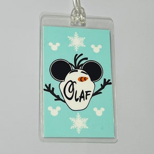 May include: A blue and white plastic luggage tag featuring a cartoon Olaf from Frozen wearing Mickey Mouse ears. The tag has the text "Olaf" on it and is surrounded by snowflakes and Mickey Mouse heads.