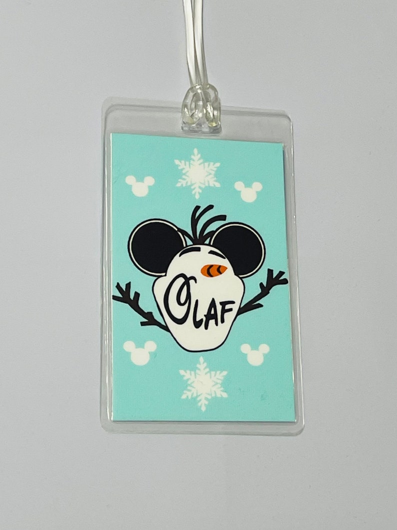 May include: A blue and white plastic luggage tag featuring a cartoon Olaf from Frozen wearing Mickey Mouse ears. The tag has the text "Olaf" on it and is surrounded by snowflakes and Mickey Mouse heads.