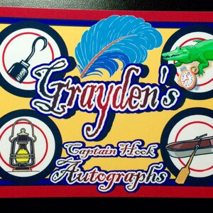 May include: A spiral-bound autograph book with a red and blue border. The cover features the name "Grayden's" in a stylized font, along with "Captain Hook Autographs." Illustrations include a hook, a feather, an alligator, a lantern, and a rowboat.