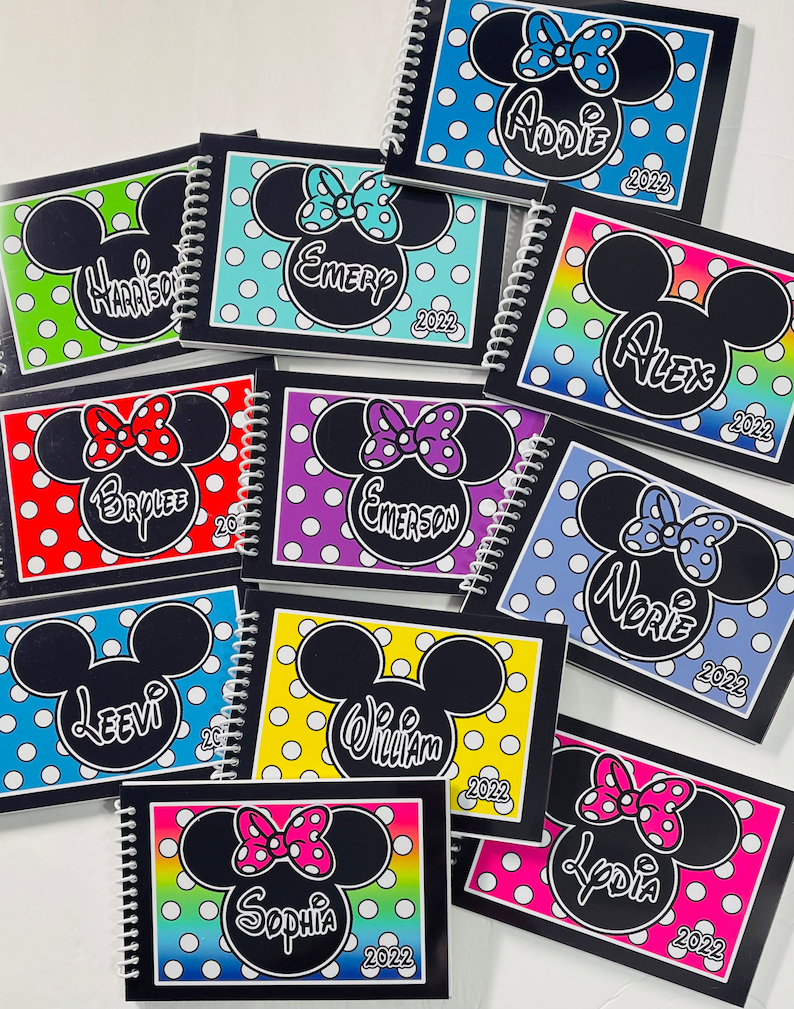 Op de afbeelding: Een verzameling van tien gepersonaliseerde spiraalnotitieblokken met een Mickey Mouse of Minnie Mouse ontwerp. Elk notitieblok heeft een andere achtergrondkleur en een andere naam die op de voorkant is gedrukt. De namen zijn: Harrison, Emery, Alex, Brylee, Emerson, Leevi, William, Norie, Sophia en Lydia. Het jaar 2022 is op elk notitieblok gedrukt.