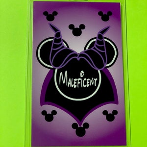 May include: Purple and black Maleficent-themed Disney character lanyard with a Mickey Mouse head silhouette. The character's horns are visible on the top of the head. The word "Maleficent" is written in white inside a black circle.