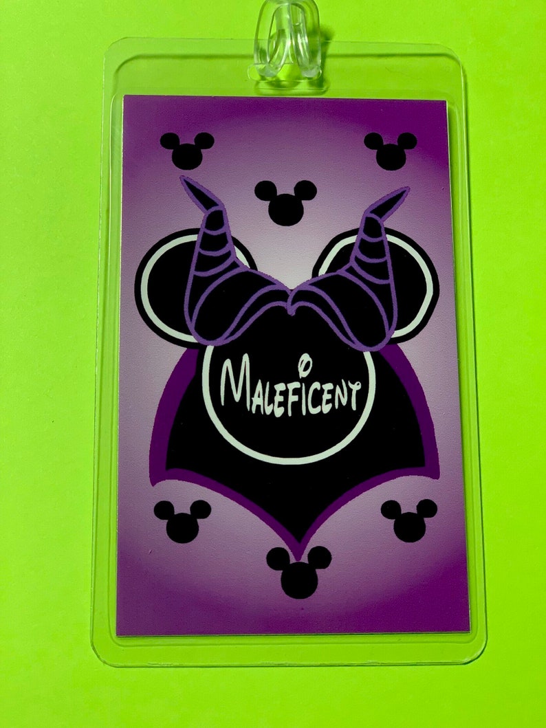 May include: Purple and black Maleficent-themed Disney character lanyard with a Mickey Mouse head silhouette. The character's horns are visible on the top of the head. The word "Maleficent" is written in white inside a black circle.