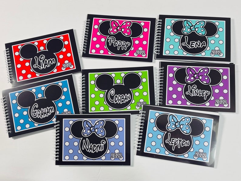 Pode incluir: Oito cadernos negros com espiral e capas de bolinhas coloridas e orelhas do Mickey Mouse. Cada caderno tem um nome diferente na capa, incluindo Liam, Poppy, Lena, Corban, Linley, Graham, Naomi e Lepton. O ano de 2022 est&aacute; impresso em cada caderno.