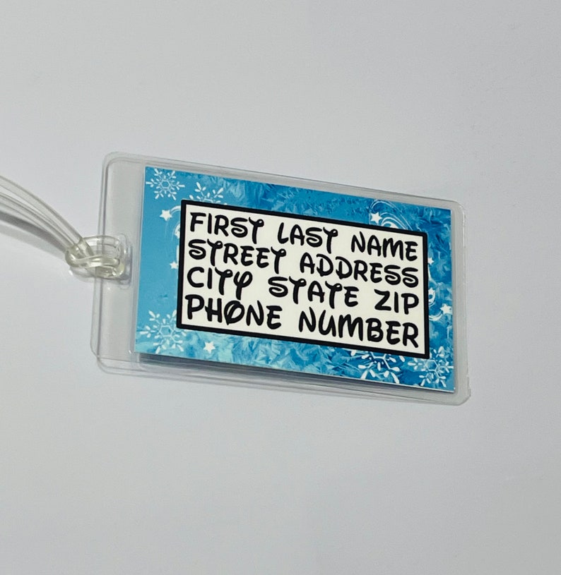 May include: A clear plastic luggage tag with a blue and white snowflake pattern. The tag has black text that reads "FIRST LAST NAME STREET ADDRESS CITY STATE ZIP PHONE NUMBER".