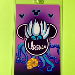 May include: A purple and blue Disney-themed lanyard with a black Mickey Mouse head featuring Ursula from The Little Mermaid. The image includes the text "Ursula" and a seashell.