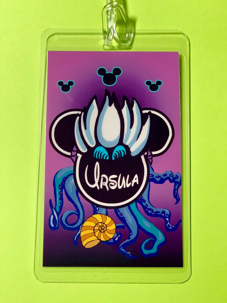 May include: A purple and blue Disney-themed lanyard with a black Mickey Mouse head featuring Ursula from The Little Mermaid. The image includes the text "Ursula" and a seashell.